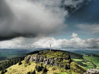 Cross on rocky mountain against cloudy sky