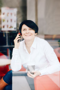 Woman talking over smart phone in cafe seen through window