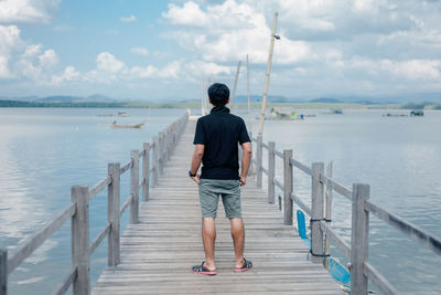 Rear view of man standing on pier over sea