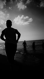 Rear view of silhouette men standing on beach against sky