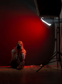 Woman sitting in a photo studio with a camera against a red light background