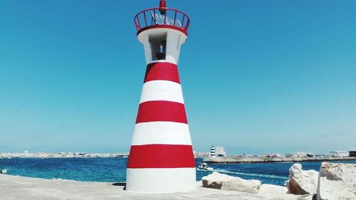 Lighthouse by sea against clear blue sky