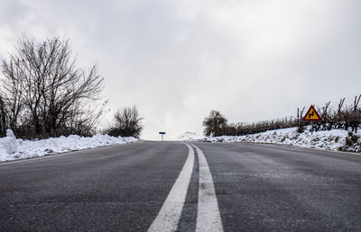 Road by trees against sky during winter