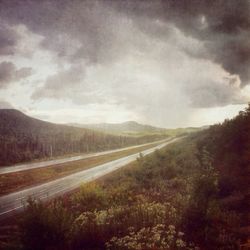 Road passing through field against cloudy sky