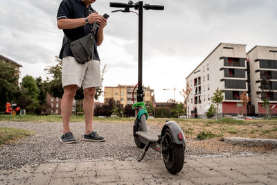 Commuter hipster man with electric scooter using smartphone in the suburbs. eco transport concept 