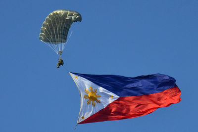 Low angle view of person paragliding with philippines flag against clear blue sky