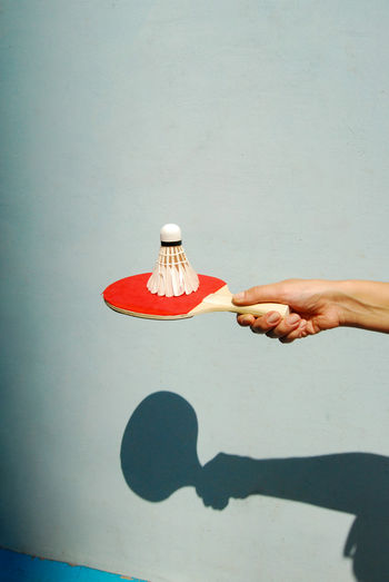 Close-up of human hand holding shuttle cock on tennis racket against wall