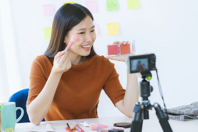 Smiling female video blogger applying in front of camera