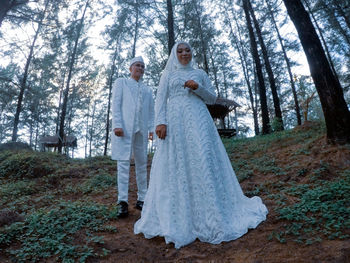 Newlywed bride and groom standing amidst trees in forest