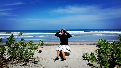 Teenage girl wearing hat while sitting at beach against blue sky