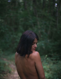 Rear view of shirtless woman standing in forest