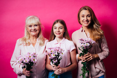 Portrait of cheerful family with flowers against pink background