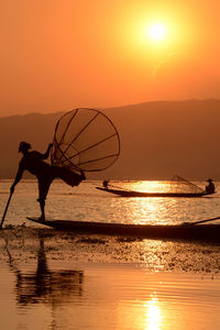 Silhouette men fishing in lake during sunset