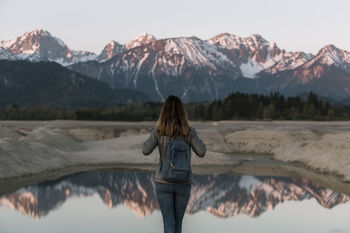 REAR VIEW OF WOMAN STANDING ON SNOWCAPPED MOUNTAIN