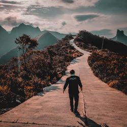 Rear view of man walking on footpath against sky