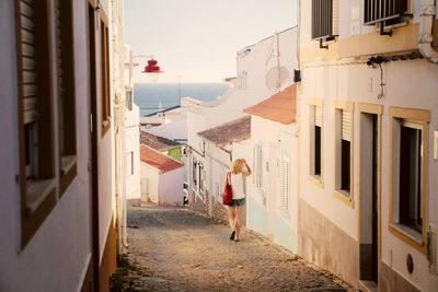 Rear view of woman walking on footpath amidst buildings in city