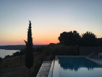 Swimming pool by lake against sky during sunset