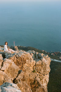 Woman sitting on cliff against sea