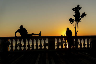 Silhouette people standing by railing against sky during sunset