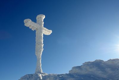 Low angle view of cross on rock against clear blue sky