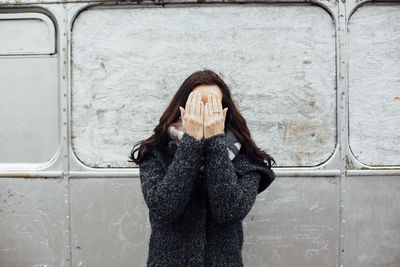 Young woman covering face against vehicle
