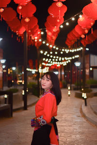 Woman standing by illuminated lights at night