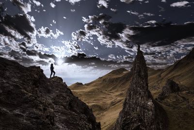 Low angle view of silhouette person standing on rocky mountains against cloudy sky