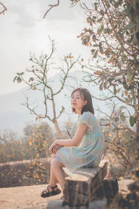 Side view of a young woman sitting against trees