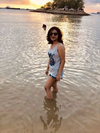 Portrait of smiling young woman standing in sea during sunset