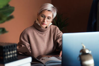 Fashion woman in brown oversize sweater working in modern work place or office with laptop