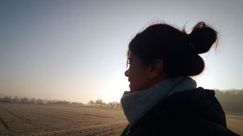 Side view of woman looking at view on field against sky during sunset