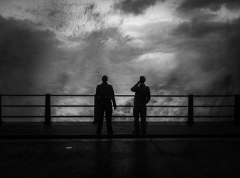 Rear view of men walking on railing against sky