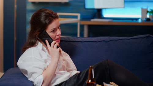 Young woman using mobile phone while sitting on laptop