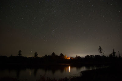 Silhouette trees by lake against sky at night