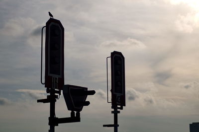 Low angle view of silhouette bird perching on pole against cloudy sky