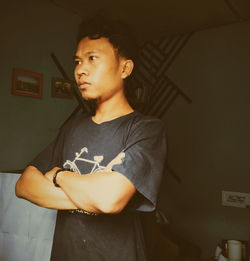 Young man looking away while standing against wall at home