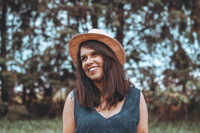 Thoughtful young woman wearing hat while standing against trees