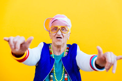 Portrait of smiling senior woman dancing against yellow background