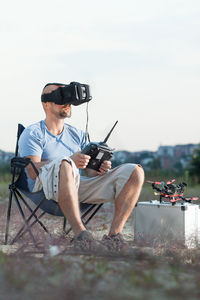 Full length of man using virtual reality simulator while sitting on chair