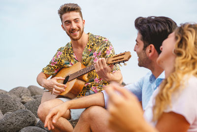 Group of people playing guitar and singing in the seaside on summer