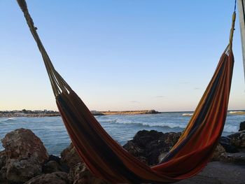 Hammock hanging at beach against sky during sunset