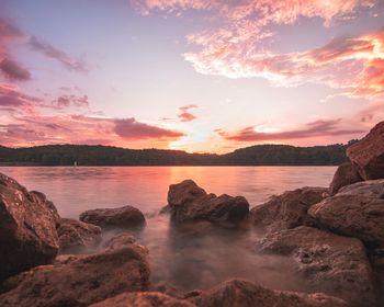 Rocks by sea against sky during sunset