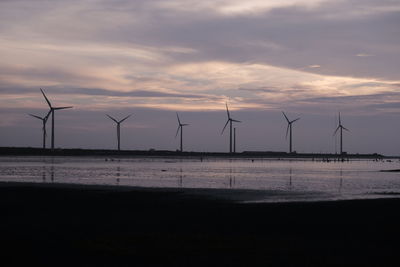 Wind turbines on field against sky during sunset