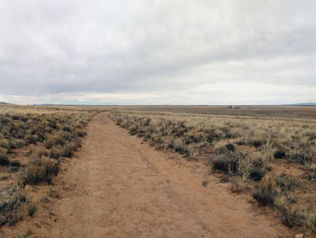 Dirt road passing through landscape against sky