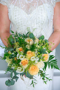 Midsection of woman holding flower bouquet against wall