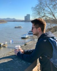 Side view of young man looking away while holding coffee cup in city