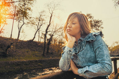 Mid adult woman looking away while sitting against sky during sunset