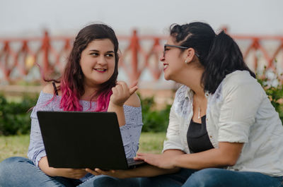 Friends discussing while working on laptop at park