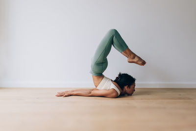 Yoga teacher practicing yoga position of locust against white wall and wood floor with copy space