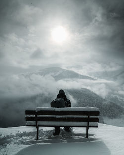 Rear view of person sitting on bench in snow